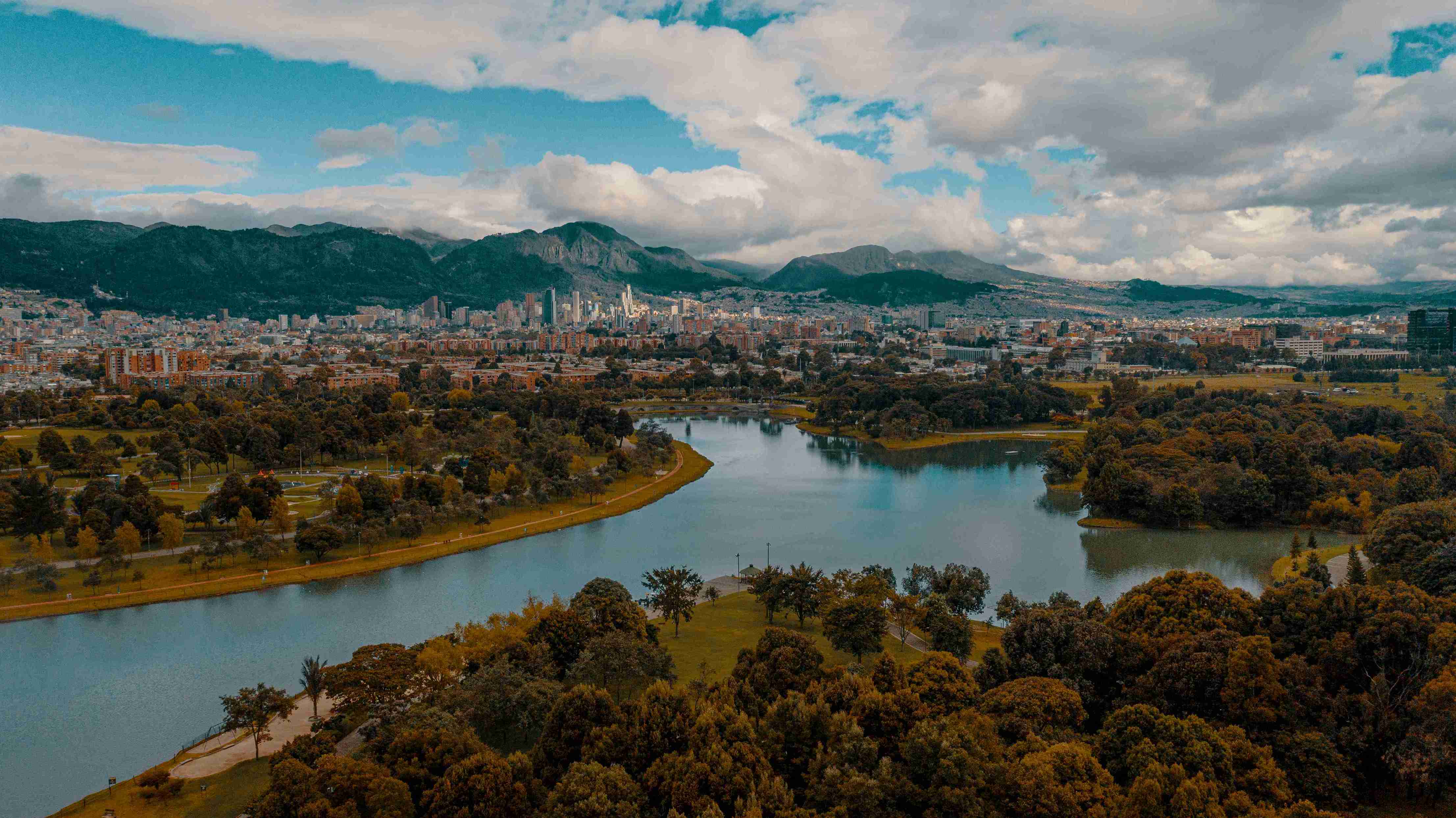 Panorámica del Parque Simón Bolívar en Bogotá. Se observa el lago central rodeado de árboles, senderos verdes y, al fondo, la ciudad con sus cerros orientales. Foto: Ricardo Baez - Archivo IDT