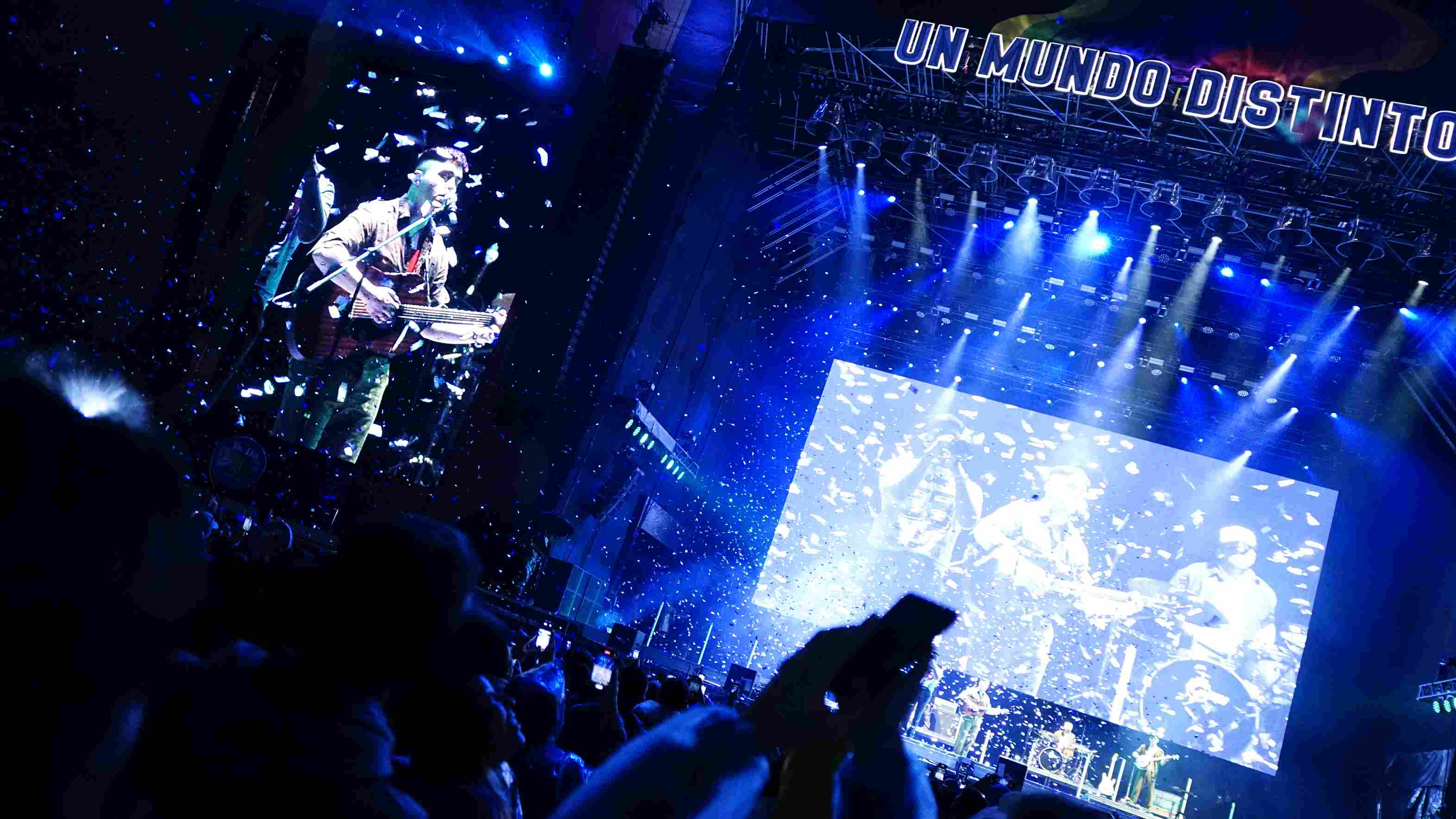 Una multitud de siluetas graba una actuación de noche en un escenario con luces azules. El confeti azul cae. Fotografía Archivo IDT